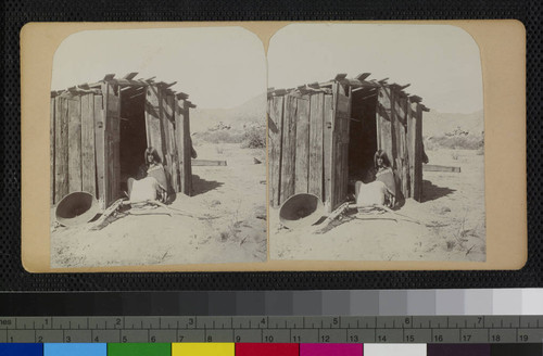 Hualapai Indian woman in doorway of house. A large basket is at the left