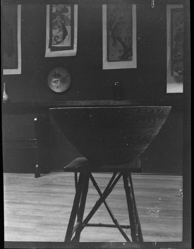 View of a basket on stand, photographed in a gallery with Asian art