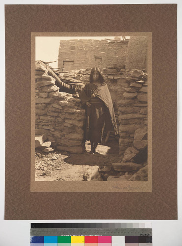 A young Hopi woman standing among pueblo walls, Oraibi, Arizona