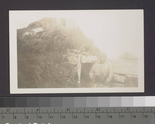 Native man beside dwelling