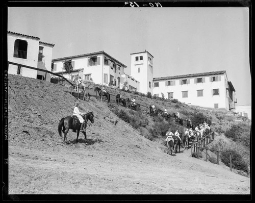 Boys riding horses toward campus buildings, Urban Military Academy, Brentwood, Los Angeles