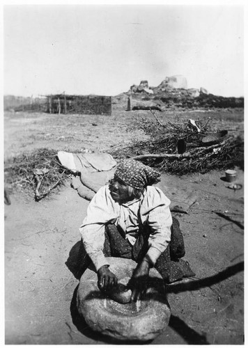 Coahuilla Indian woman grinding corn in stone mortar