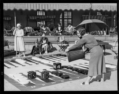 Woman rolling giant dice in giant backgammon game, Santa Monica