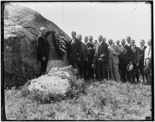 Plaque dedication with unidentified group of men unveiling a plaque on a rock
