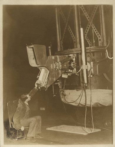 Paul W. Merrill seated beside a spectrograph mounted on the 60-inch telescope, Mount Wilson Observatory