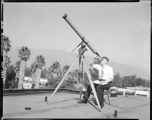 Robert Richardson looking through a small refracting telescope, seated on a rooftop on Santa Barbara Street, Pasadena