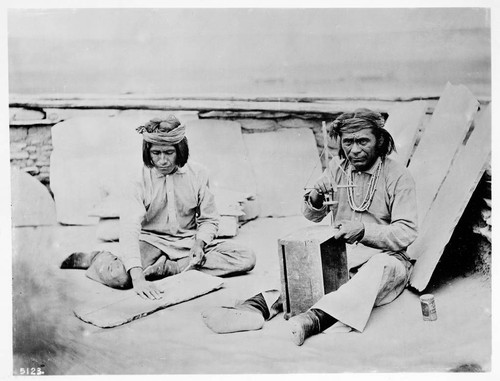 Zuni making wampum necklace. Boy making cord for same