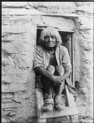 Hopi man in doorway, with his feet on ladder