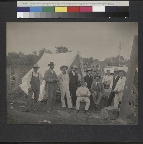 Group of 10 men gathered in front of a canvas tent, with astronomical instruments near them