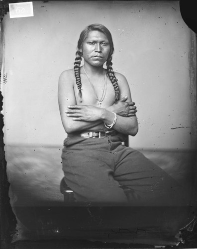 Portrait of a Shoshone man, seated and wearing a cross on a chain around his neck