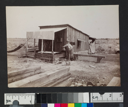 Man in front of wooden house in unidentified settlement