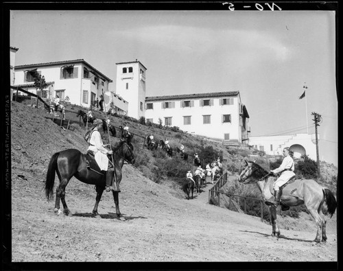 Boys riding horses toward campus buildings, Urban Military Academy, Brentwood, Los Angeles