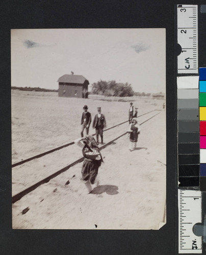 A railroad worker, Native American women, and others walking along railroad tracks