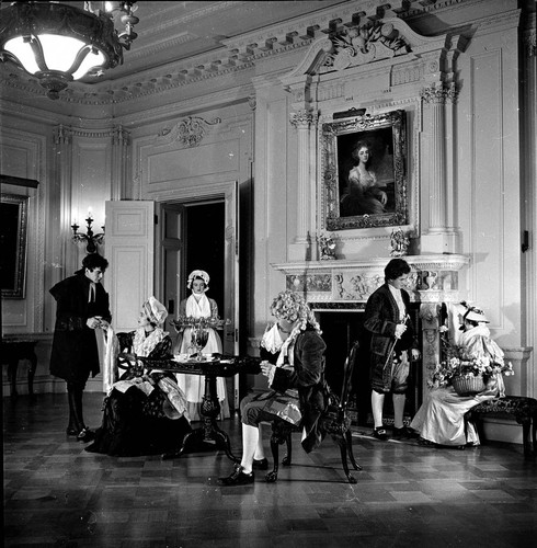 Six people in period costume around tea table in dining room in the Huntington residence (Victor Mature on left, Frederick Blanchard seated)