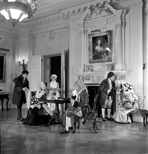 Six people in period costume in the dining room in the Huntington residence