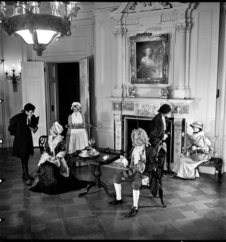 Six people in period costume around tea table in dining room in the Huntington residence