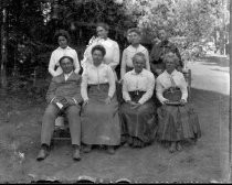 Group portrait of one man and 7 women on chairs outdoors, c. 1912