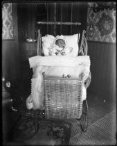 Baby in wicker carriage, with pacifier