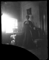 Woman posing next to chair, in front of window