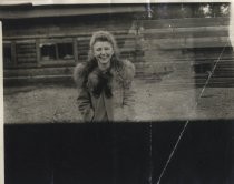 Ruby Levin in front of log cabin, wearing fur-trimmed coat