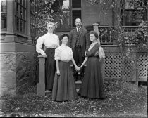 Three women and one man outside brick building, c. 1912