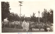 Two boys dressed in overalls standing in front of a flower garden