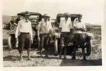 Four men barefoot in the desert with automobiles