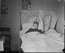 Woman lying in bed with lace on headboard, c. 1912