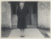 Ruby Levin in coat, standing in front of concrete building