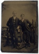 Portrait of two men posing against a fence