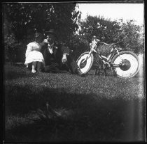 Man with young girl sitting on grass next to bicycle