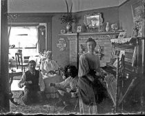 Woman at piano, men playing cards in parlor, c. 1912