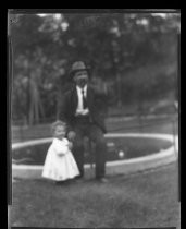 Man in hat, seated outdoors, with small child