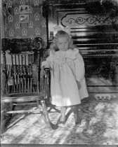 Young girl in ruffled dress with rocking chair and piano, c. 1912
