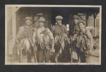 Five men with rifles and game birds in front of cabin