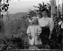 Three women and a child outside house, with hills, c. 1912