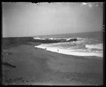 Three people on a stretch of beach, with rocky outcrop