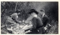 Two women and a man around a campfire