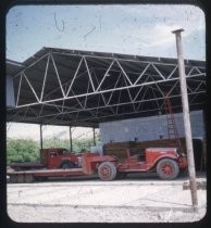 Red pick-up truck and flat bed parked in metal shed