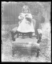 Young child standing in upholstered chair, holding kittens