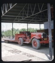 Red pick-up truck and flat bed parked in metal shed