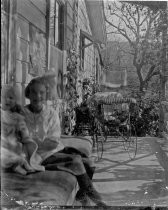 Girl seated with baby and carriage outside house, c. 1912