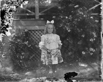 Young girl in ruffled dress outdoors with trellis, c. 1912