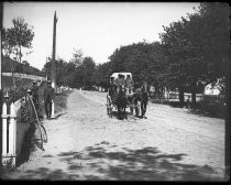 Horse-drawn coach on dirt road with picket fences