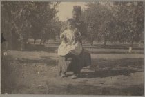 Photo from the Von Dorsten family album.Woman seated in orchard holding Chinese (?) baby on lap