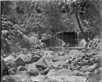 Water flowing over dam into rocky stream, c. 1912