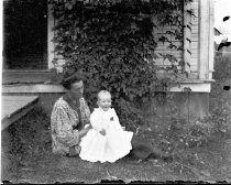 Woman with baby on lawn in front of house with vine, c. 1912