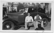 Two young men sitting on running board of two door coupe with top up