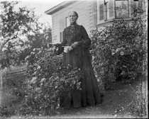 Woman posing with rose bushes in black dress, c. 1912