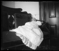 Baby in gown, lying on settee